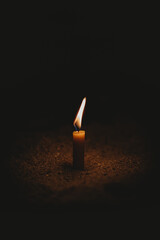 Wall Mural - Small candle burning on the soil ground in the dark - light contrast concept