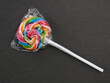 single colorful lollipop wrapped in plastic packaging on black background, top view