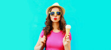 Portrait Of Happy Young Woman With Ice Cream Blowing Her Lips Wearing Summer Straw Hat On Blue Background