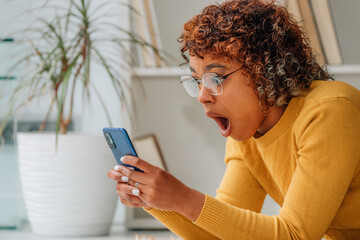 girl at home amazed and surprised looking at mobile phone