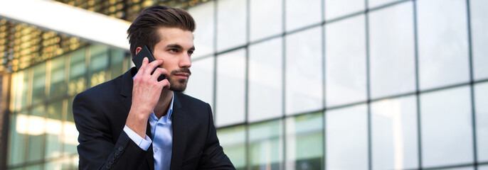 Young businessman talking on the phone in front of corporate office building