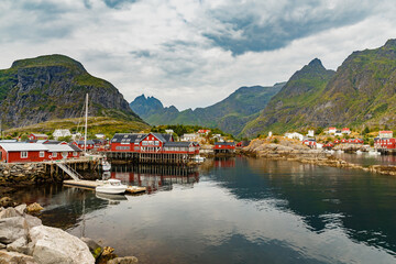 Wall Mural - Lofoten Islands, classic norwegian landscape, small fishing houses of red color on the coast, a small boats, rocky coast with dramatic sky