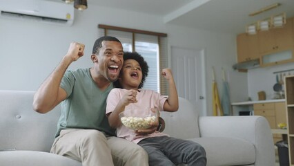 Wall Mural - Cheerful African American Father and his little boy watching and cheering sports games competition together at home, celebrate