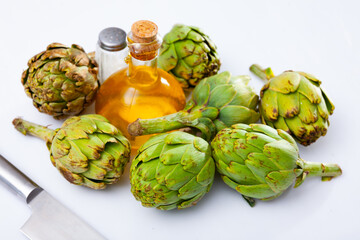 Wall Mural - Bunch of artichokes placed over white background with saltcellar and glass oil bottle.