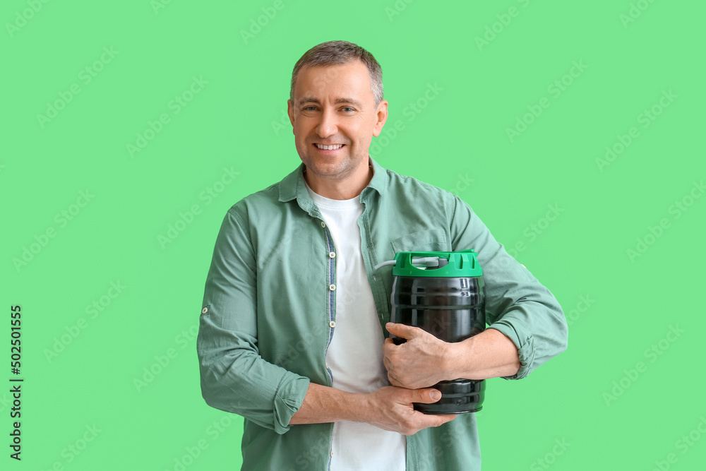 Mature man with barrel of beer on green background