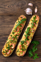 Wall Mural - Homemade baguette sandwich or pizza with shrimp, garlic fresh rocket salad and parsley. Top view photo on a wooden background with place for your text.