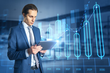 Poster - Attractive young european businessman using tablet with growing annual business chart report hologram on blurry office interior background. Analysis and company concept. Double exposure.