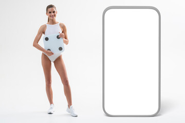 Sporty female holding weight scales next to big phone template