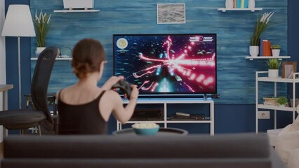 Sticker - Young woman holding wireless controller playing action space shooter disappointed because losing online game on console in front of tv. Gamer girl sitting on couch unhappy with gaming performance.