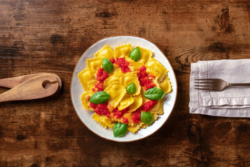 Wall Mural - Ravioli with tomato sauce and basil. A plate of stuffed pasta, shot from the top on a rustic wooden table