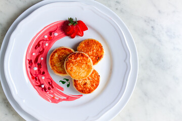 Wall Mural - Cottage cheese pancakes, on a white plate decorated with sauce, fresh strawberry berry, close-up, no people,