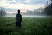 Child Boy Standing And Looking Into A Foggy Meadow
