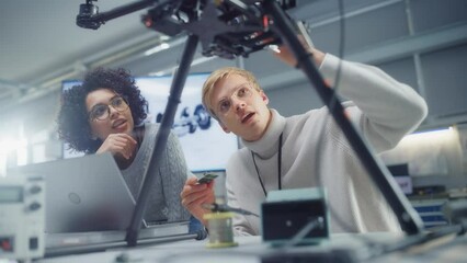 Poster - Professional Young Black Developer Coding at Laptop while her Male Colleague Holding Semiconductor at Factory Workshop. Innovative Technologies in Unmanned Aerial Vehicle Design Concept
