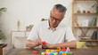 asian senior male with dementia trying to recognize and arrange color letter blocks in order at home. in-home care and brain exercise for rehabilitation concept