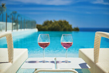 Two Glasses With Cocktails On Table Between Deck Chairs Sunbeds On The Swimming Pool, Sea And Blue Sky Background. Summer Holidays, Relaxation, Accommodation In Luxury Hotel Concept, No People. Spain