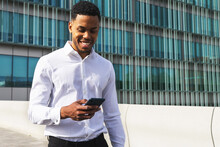 Smiling Black Businessman Browsing Smartphone On Street