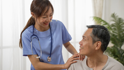 Closeup of caring Asian woman nursing aide talking and encouraging older male patient during home visit. Domiciliary care for elderly senior concept