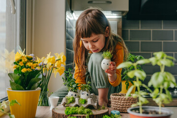 Wall Mural - Little girl making composition from eggshells with sprouts