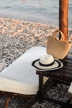 Sunbeds With Straw Umbrella On The Pebble Beach. Hat, Bag, And Glasses Equipment