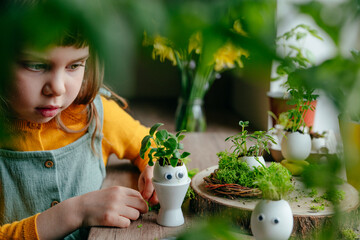 Wall Mural - Little girl decorating eggshell with toy eyes on the table