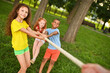 © Evgeniy Kalinovskiy - group of preschool children - boys and girls compete in a tug of war against the background of a park and greenery.