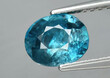 Natural gemstone blue zircon in tweezers on a gray background