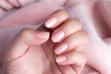 Female hand with beautiful natural manicure - pink nude nails on pale pink fluffy fabric, textile background