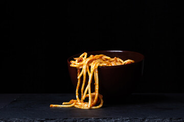 Wall Mural - Spaghetti in tomato sauce on a black background. Spaghetti falls out of the plate. traditional italian food