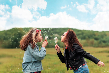 Wall Mural - Mother and daughter blow dandelions on each other. Side view. In the background, the forest and the sky. Copy space. The concept of freedom and family happiness