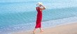Young woman in red dress and white hat walking down the sand beach on sea summer vacation