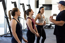 Three Woman Standing In A Row Listening To Their Fitness Trainer Before A Workout
