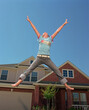 © SuperStock - Teenage girl jumping in front of home, striking a pose mid air