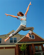 © SuperStock - Teenage girl jumping in front of home, striking a pose mid air