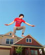 © SuperStock - Teenage boy jumping in front of home, striking a pose mid air