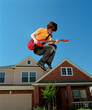 © SuperStock - Teenage boy with guitar jumping in front of home, striking a pose mid air