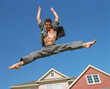 © SuperStock - Young man jumping in front of home, striking a pose mid air