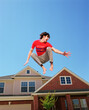 © SuperStock - Teenage boy jumping in front of home, striking a pose mid air