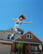 © SuperStock - Teenage girl jumping in front of home, striking air guitar pose mid air