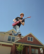 © SuperStock - Teenage boy with guitar jumping in front of home, striking a pose mid air