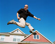 © SuperStock - Middle aged man jumping in front of home, striking a pose mid air