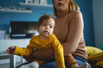 Wall Mural - One small caucasian baby girl happy with in hands of her mother holding her at home in front of blue wall in day real people front view copy space family bonding leisure concept