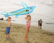 © SuperStock - Young children holding up inflatable dolphin and laughing at the beach