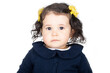 Adorable one year old baby girl headshot over white background. She has long curly hair and uses yellow rose hair clips. She is looking at the camera. 