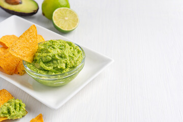 Wall Mural - Mexican guacamole homemade healthy vegetarian dip, spread, or salad made of mashed ripe green avocado served in glass bowl as snack or appetizer on white wooden table with lime. Image with copy space