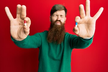 Sticker - Redhead man with long beard holding two different pills looking at the camera blowing a kiss being lovely and sexy. love expression.