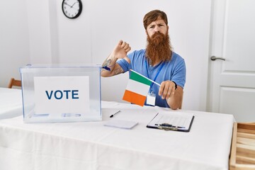 Poster - Caucasian man with long beard at political campaign election holding ireland flag with angry face, negative sign showing dislike with thumbs down, rejection concept