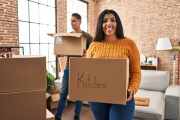 Poster - Young couple moving to a new home with cardboard boxes sticking tongue out happy with funny expression.