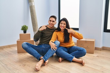 Canvas Print - Young couple sitting on the floor at new home smiling cheerful showing and pointing with fingers teeth and mouth. dental health concept.