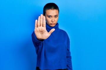 Wall Mural - Beautiful hispanic woman with short hair wearing turtleneck sweater doing stop sing with palm of the hand. warning expression with negative and serious gesture on the face.