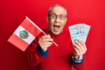 Poster - Handsome senior man with grey hair holding peru flag and peruvian sol banknotes celebrating crazy and amazed for success with open eyes screaming excited.